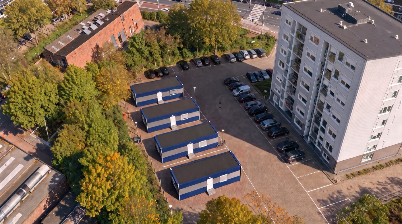 Luchtopname van de acht logeerwoningen, twee aan twee, naast de flat.